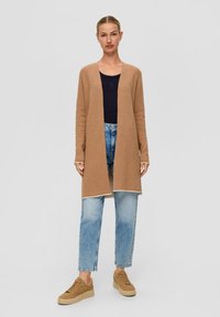 Cardigan long ouvert en tricot beige, associé à un haut bleu marine et à un jeans droit bleu clair. Présente un design et une texture minimalistes.
