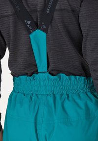 Turkoise skibroek met verstelbare zwarte bretels en een elastische tailleband, gemaakt van lichtgewicht, gestructureerde stof voor optimale bewegingsvrijheid.