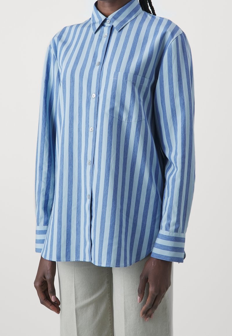 Chemise à manches longues rayée bleu clair et blanc avec un col boutonné et une poche poitrine, confectionnée dans un tissu doux, présentant une coupe décontractée.