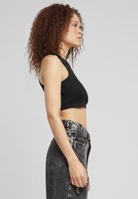 Fekete bordázott croptop széles vállpántokkal, magasderekú, fakó fekete farmernadrággal párosítva, amelyen látható varrások és zsebek találhatók.
