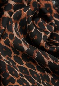 Leopardprint stof i nuancer af brun og sort, med en glat tekstur og flydende folder, der fremhæver tydelige dyrelignende mønstre.