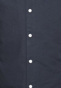 Camicia button-up di un blu navy scuro con una texture liscia, caratterizzata da bottoni bianchi lungo il davanti e un design del colletto standard.