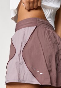Pantalones cortos deportivos en dos tonos de malva con un acabado texturizado, que presentan costuras curvas y detalles reflectantes en el dobladillo.