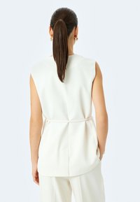 Beiger ärmelloser Top mit figurbetontem Schnitt, glattem Stoff und einem Taillengürtel. Minimalistisches und sauberes Design.