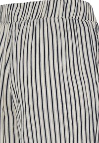 Gros plan sur un tissu à rayures verticales noires et blanches avec une ceinture élastique froncée, probablement partie d'une jupe ou d'un pantalon.