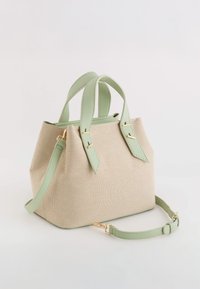 Beige canvas tas met groene leren accenten, korte handvatten en een afneembare schouderriem. Textuurstof en details van gouden hardware.