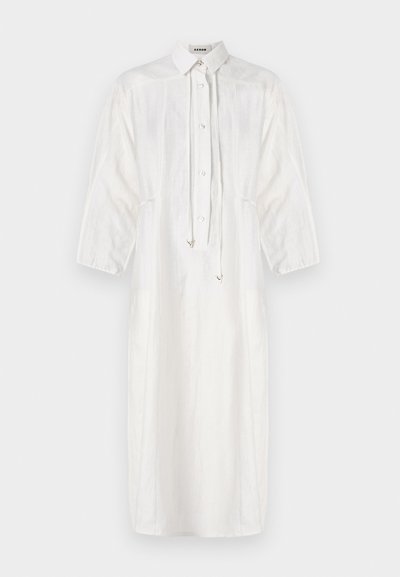 Abito bianco in lino con colletto, chiusura con bottoni e dettagli con cordino. Presenta maniche lunghe e una silhouette midi rilassata.