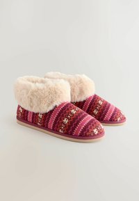 Pūkaini rozā un sarkana rakstaina šļūcene ar mīkstu krēmkrāsu mākslīgu kažokādu un gaišas brūnas gumijas zoli, piedāvājot siltu un ērtu dizainu.