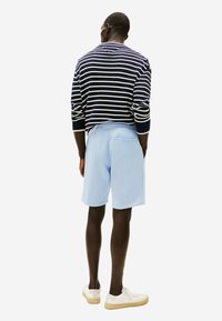 Pull rayé bleu marine et blanc, shorts bleu clair, baskets blanches avec semelles beiges. Vue de dos, mettant en avant une coupe décontractée et confortable.
