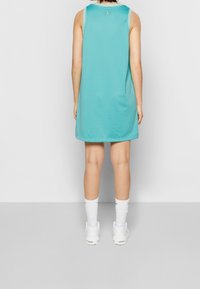 En ärmlös turkos sportklänning med en texturerad meshdesign, med en logotyp på ryggen, kombinerad med vita strumpor och sneakers.