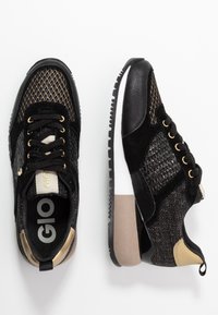 Czarno-złote sneakersy z siateczkowych i zamszowych materiałów, z teksturowanymi akcentami, wyściełaną białą i kawową podeszwą oraz czarnymi sznurówkami.