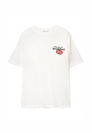 T-shirt bianco a maniche corte con testo nero "L'Arte della Colazione!" e etichetta rossa con la scritta "Vitamina C e Carboidrati, Per Favore" sul petto.