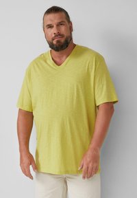 T-shirt z dekoltem w kształcie V i krótkim rękawem w jasnym żółtym odcieniu, wykonany z miękkiej, teksturowanej tkaniny; luźny krój w swobodnym stylu.