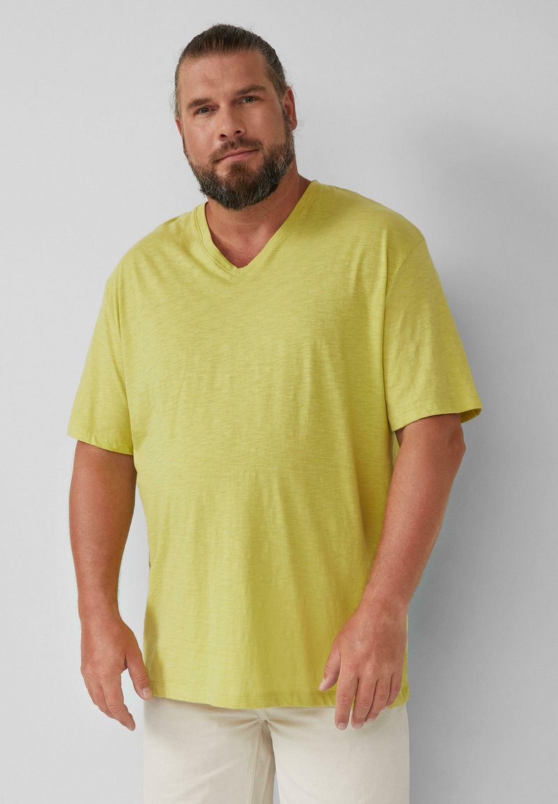 T-shirt z dekoltem w kształcie V i krótkim rękawem w jasnym żółtym odcieniu, wykonany z miękkiej, teksturowanej tkaniny; luźny krój w swobodnym stylu.