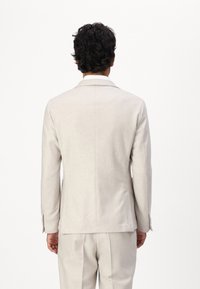 Sacou bej deschis, cu o croială ajustată, rever tăiat și mâneci lungi. Material neted, detalii minimale de coasere și o formă structurată.
