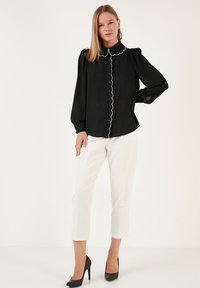 Black blouse with a scalloped white collar, button-down front, and puffed long sleeves, paired with white cropped pants and black heels.