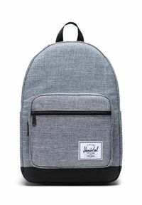 Sac à dos en tissu gris à forme arrondie, poche avant zippée, base noire et étiquette blanche avec le nom de la marque. Matière texturée pour plus de durabilité.