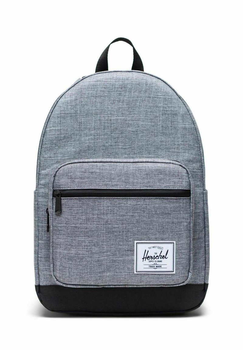 Sac à dos en tissu gris à forme arrondie, poche avant zippée, base noire et étiquette blanche avec le nom de la marque. Matière texturée pour plus de durabilité.