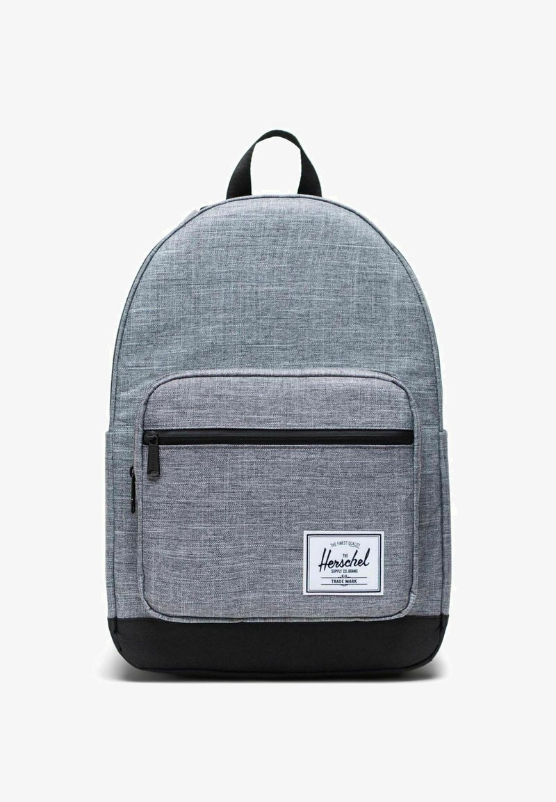 Sac à dos en tissu gris à forme arrondie, poche avant zippée, base noire et étiquette blanche avec le nom de la marque. Matière texturée pour plus de durabilité.