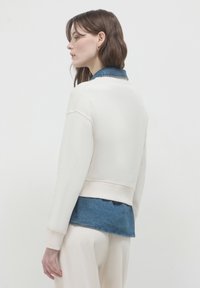 Felpa corta con una morbida texture color crema, dotata di un colletto blu denim. Il design include maniche a vestibilità rilassata e un look a strati.