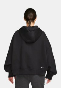 Svart oversize hoodie med en känguruficka, stor huva och ribbade manschetter, med en liten vit Nike-logotyp nederst till vänster.