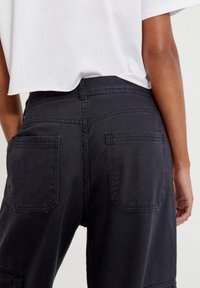 Mustat farkkucargo-housut, joissa on takataskut ja näkyvä ompelu, yhdistettynä lyhytmalliseen valkoiseen toppiin, joka näyttää rennolta ja teksturoidulta.