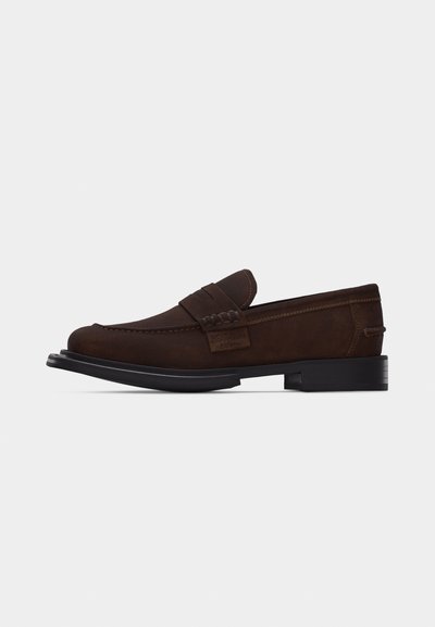 Mocassin à enfiler en cuir marron avec détails surpiqués et semelle noire, présenté de profil sur un fond blanc uni.