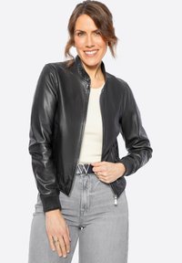 Černá kožená bombardér bunda se zipovým zapínáním, žebrovanými manžetami a stojáčkem, v kombinaci s šedými džíny s vysokým pasem a opaskem s přezkou ve tvaru písmene "W".