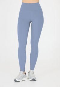 Höga leggings i ett mjukt ljusblått tyg, med två sidfickor, slät textur och en figurnära silhuett.
