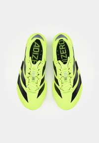 Bright yellow athletic shoes with black stripes, featuring a textured upper, reinforced toe cap, and prominent branding. Designed for performance.