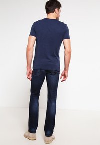 T-shirt a girocollo navy, maniche corte, abbinato a jeans blu scuri. Tasche visibili, vestibilità slim, texture morbida. Footwear casual beige.