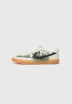 Nízké tenisky s béžovým semišovým lemem, zelenou květinovou textilií, černým logem Nike, bílými tkaničkami a gumovou podrážkou na bílém pozadí.
