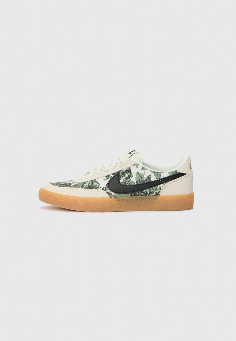 Sneaker basse con bordi in suede beige, tessuto floreale verde, logo Nike nero, lacci bianchi e suola in gomma marrone su sfondo bianco.