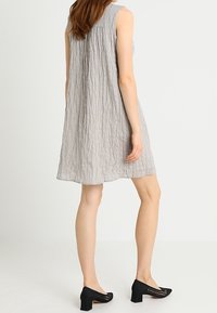 Vestido gris sin mangas con tejido texturizado, de silueta hasta la rodilla y con sutiles plisados. Combinado con zapatos de tacón ancho perforados en negro.