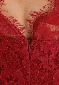 Gros plan sur un tissu en dentelle rouge avec des motifs floraux et un revêtement en maille, présentant une fermeture éclair centrale et des détails en frange délicats le long du bord.