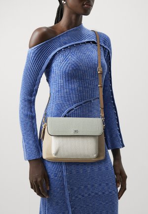 Femme noire portant une robe tricotée bleu à une épaule et portant un sac crossbody texturé beige et crème avec une sangle marron.