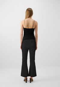 Camisole noir ajusté avec de fines bretelles et un tissu texturé, associé à un pantalon noir évasé au fini lisse et à un subtil éclat.
