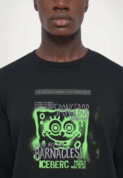 Schwarzes Baumwoll-T-Shirt mit einem bunten SpongeBob-Graphic, grünen Akzenten, Text und verspielten Designelementen. Rundhalsausschnitt, lässige Passform.