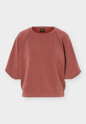 Sweat-shirt rose poudré à manches courtes et col rond avec manches raglan et ourlet côtelé, présentant un petit logo près du bord inférieur.