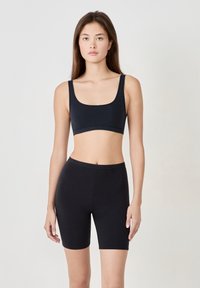 Svart kort tanktop och högmidjade shorts, båda gjorda av glatt tyg. Toppen har breda axelband och en fyrkantig halsringning.