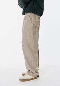 Barna kordbársony nadrág laza szabással, gumis derékkal, oldalsó és hátsó zsebekkel, fehér sportcipővel és sötét kabáttal párosítva.