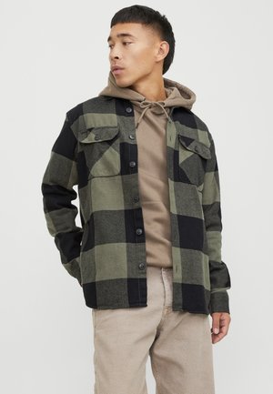 Green and black plaid shirt with button-up front, two chest pockets, and long sleeves, layered over a beige hoodie.