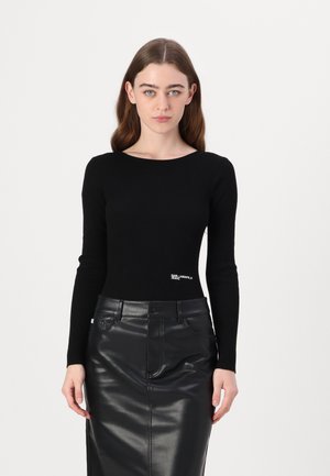 Black ribbed long-sleeve top with a round neckline and a logo detail at the waist, paired with a sleek black leather pencil skirt.