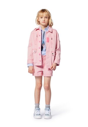 Veste en denim rose avec plusieurs poches, associée à un short assorti. En dessous, une chemise rayée bleue et des baskets blanches avec des accents bleu clair.