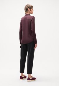 Chemise à manches longues de couleur bordeaux foncé avec un ourlet arrondi, associée à un pantalon noir rayé et des baskets bordeaux avec des accents crème.