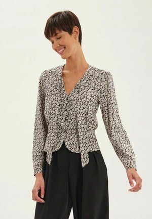 Blouse florale noir et blanc à manches longues, décolleté en V, taille cintrée et détail à nouer à l'avant. Le motif présente de petites fleurs.
