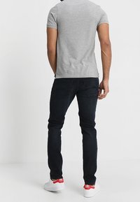 Grå kortärmad skjorta, mörkblå jeans och vita sneakers med röda detaljer. Rakt snitt med bakfickor synliga.