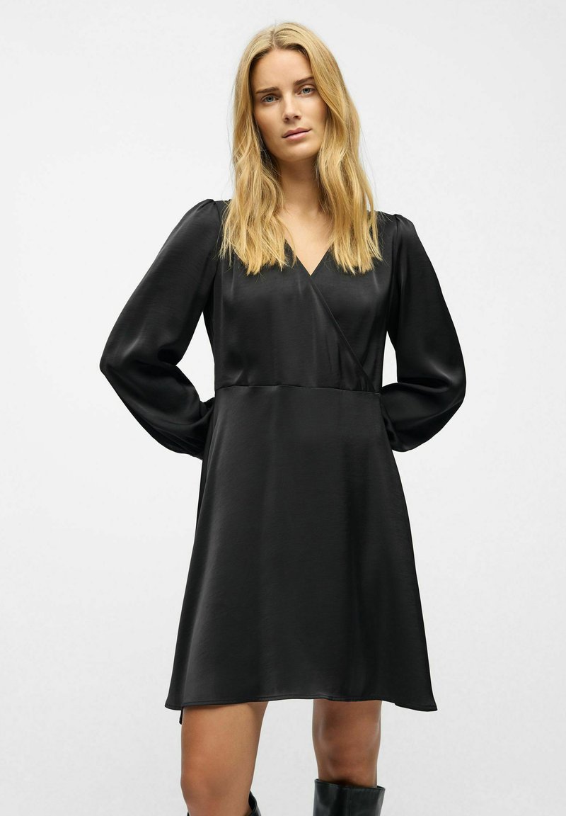 Sort satin kjole med V-hals, lange puffærmer og A-line silhuet, der har en glat tekstur og minimal detaljering.