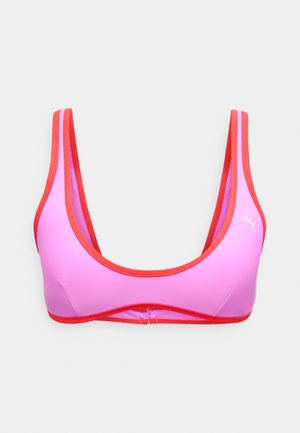 Brassière de sport rose avec bordure rouge et fines bretelles, arborant un petit logo Puma blanc sur le côté gauche.