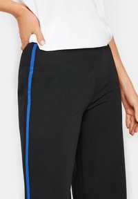 Zwarte broek met een zijstreep in felblauw. Het materiaal lijkt soepel met een ontspannen pasvorm. Inclusief zijzakken en een eenvoudig ontwerp.